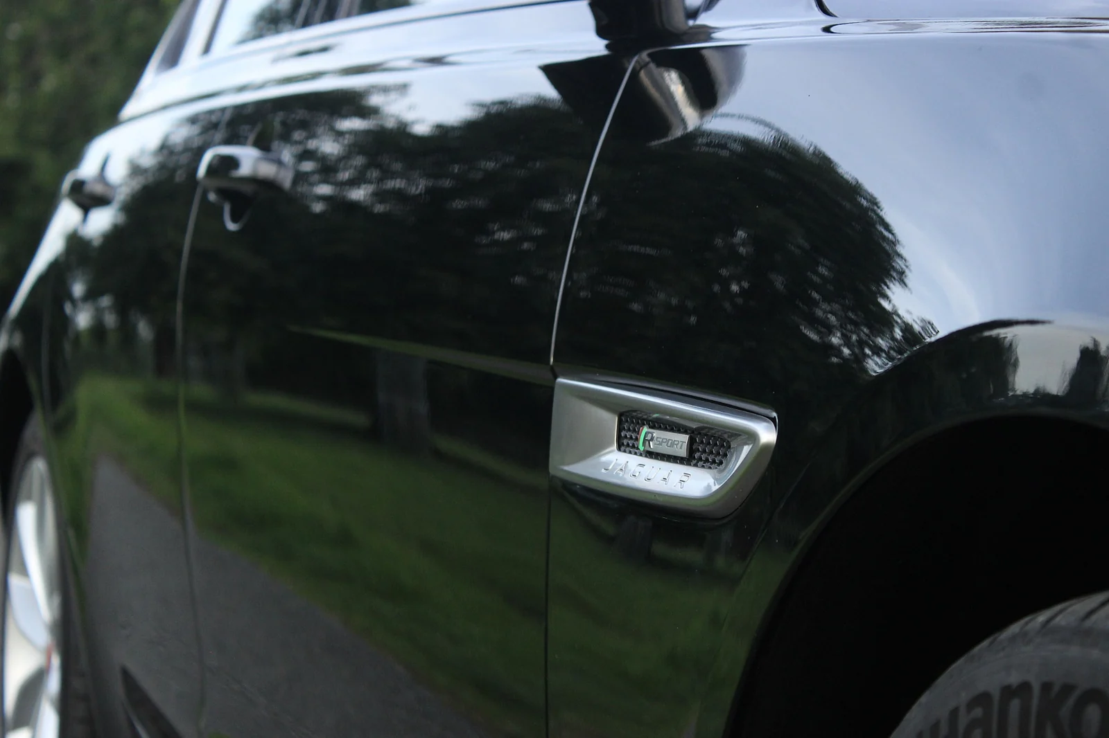 The side vent and bodywork of a black Jaguar reflecting nearby trees.