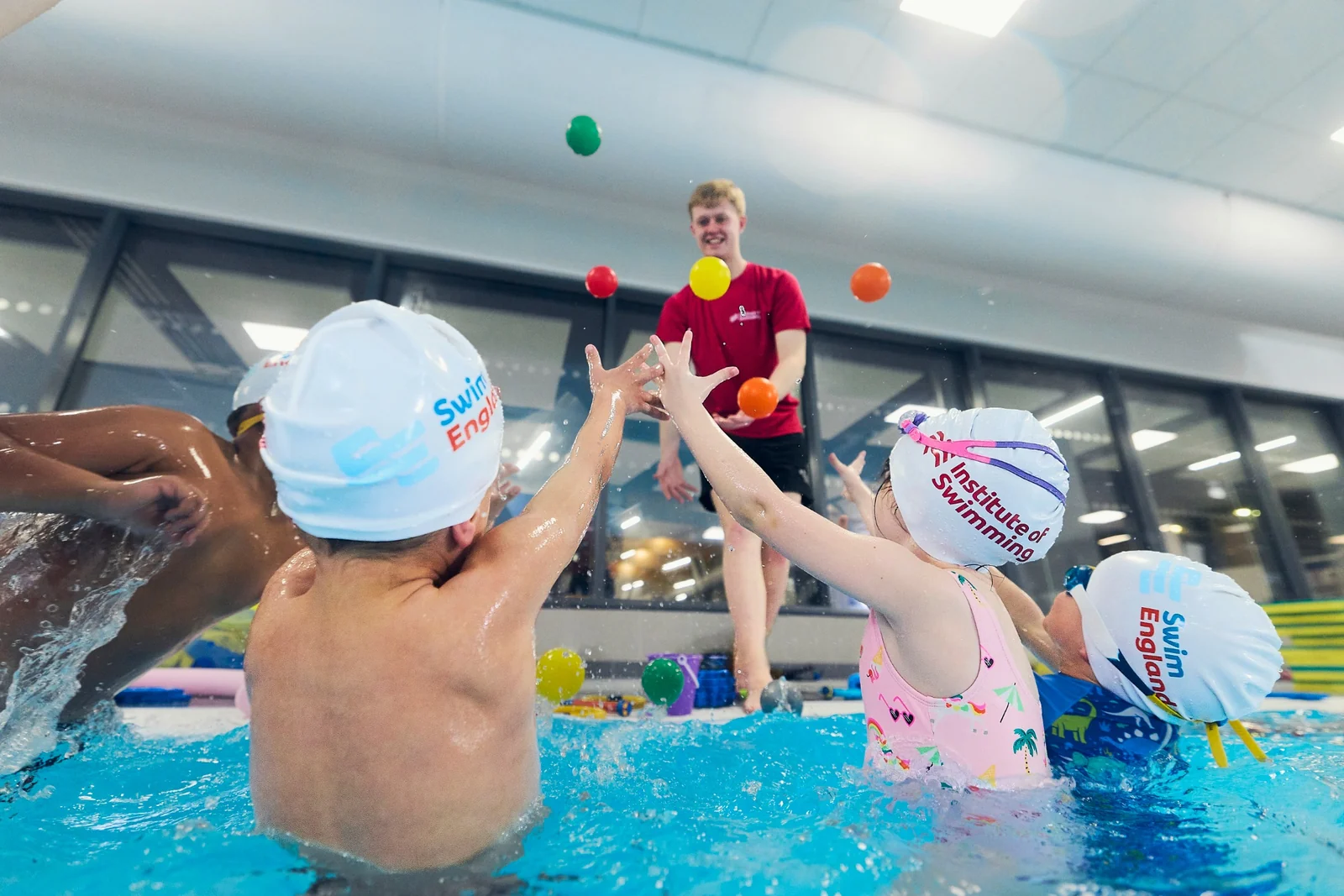 Swimmers taking part in a ball activity with Jack Ruddle beside the pool.